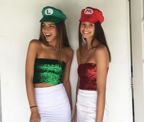 Duas mulheres de pele clara e saia branca, sendo uma de verde com boné do Luigi e uma de cropped vermelho com boné do Mário