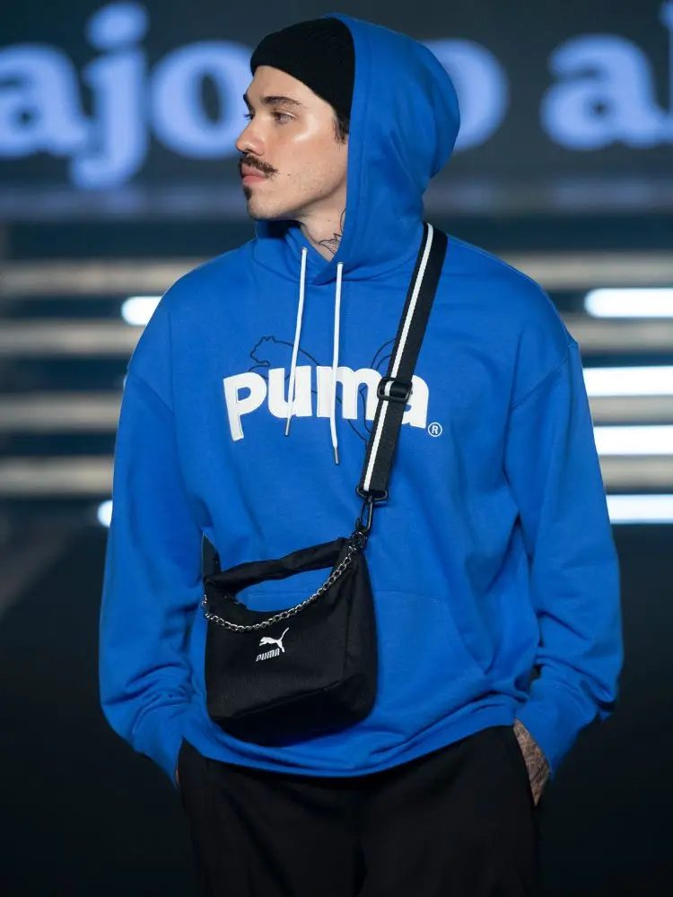 modelo no desfile do Studio 78 usando blusa azul, bolsa, calça e touca pretas, todas da Puma. 