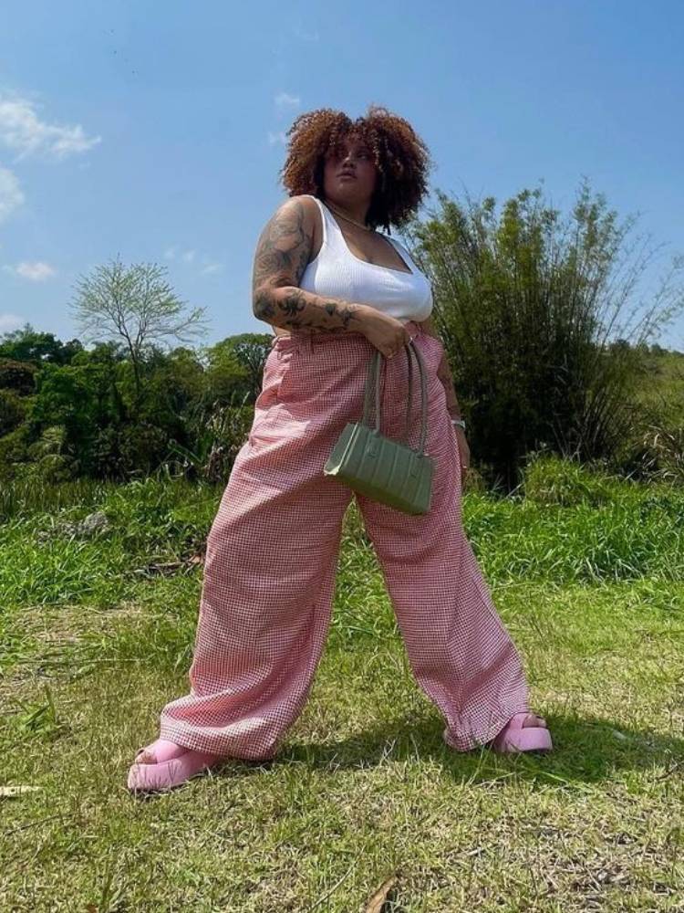 mulher usando regata branca canelada com calça vermelha xadrez e sapato rosa
