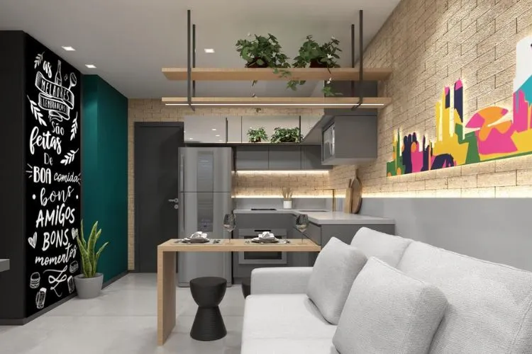 Studio com parede verde, parede preta com escritos em branco, sofá cinza, sala integrada com cozinha, plantas em prateleira e iluminação indireta, além de mesmo piso na sala e na cozinha