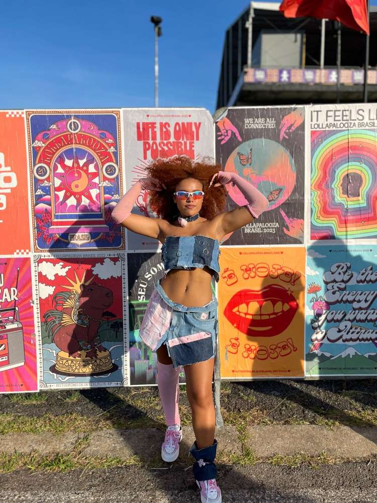 Mulher de pele negra usando cropped e saia all jeans, com luvas rosas e tênis