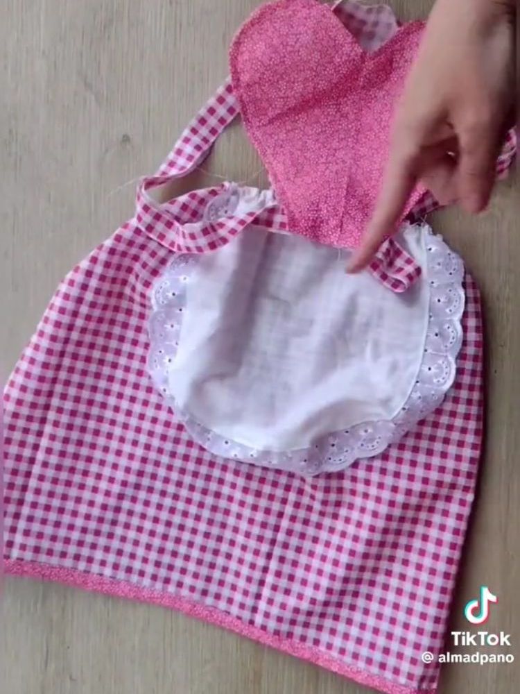 Pessoa de pele clara pontando para junção de tecido rosa em formato de coração e saia xadrez branca e rosa