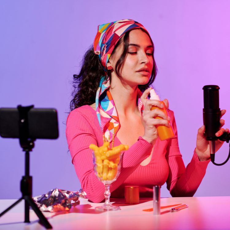 Influencer gravando conteúdo em ambiente iluminado, com celular e microfone. Ela segura um produto cosmético enquanto explica sua aplicação. Essa cena reflete o que fazem os influencers: criar conteúdo autêntico, promover produtos e engajar seu público de forma criativa.
