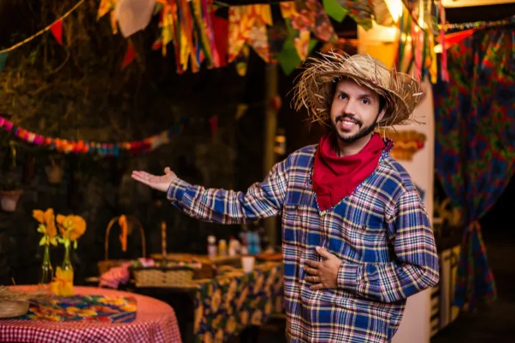 Homem de pele clara com camisa xadrez azul, lenço vermelho, chapéu de palha em festa junina 