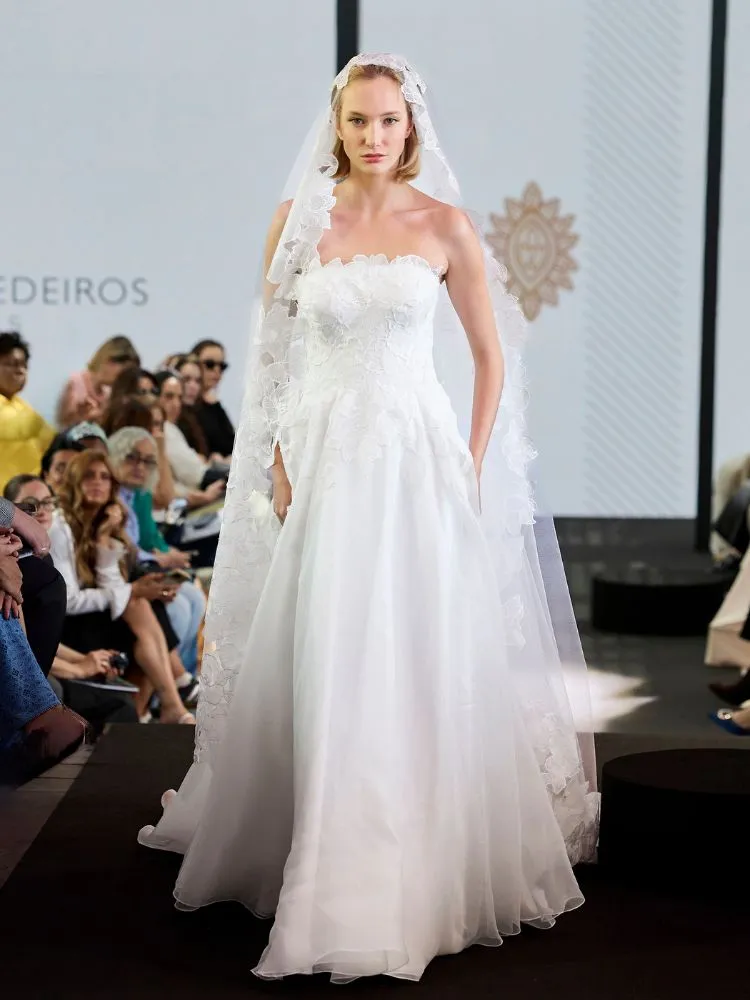 Mulher de pele clara desfilando com vestido de noiva sem alças e grinalda de flor