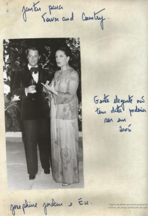 Imagem em preto e branco de Guilherme Guimarães nos anos 80 posando em pé vestido de smoking preto e gravata borboleta preta em um jantar para a Town & Country ao lado de Josephine Jordan Imagem em preto e branco de Guilherme Guimarães nos anos 80 posando em pé vestido de smoking preto e gravata borboleta preta em um jantar para a Town & Country ao lado de Josephine Jordan