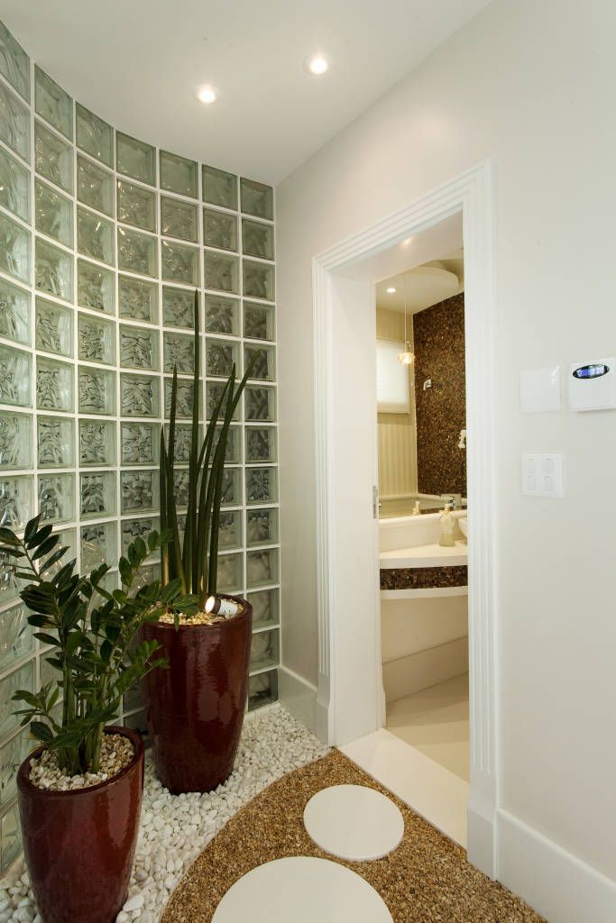 Jardim de inverno com vasos grandes em corredor com parede de azulejos com vidro, na porta de um lavabo 