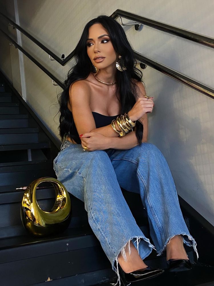 Mulher de pele clara sentada em escada usando tube top preto e calça jeans com barra desfiada