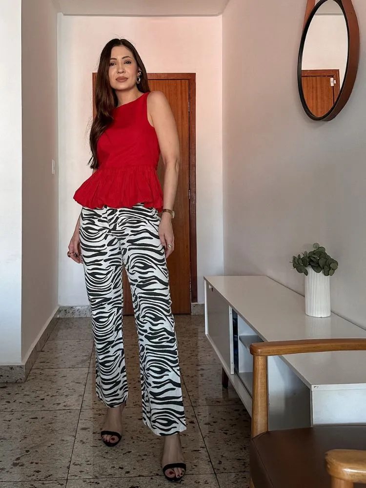 Mulher de pele clara usando blusa vermelha balonê, calça de zebra e sandália de salto 
