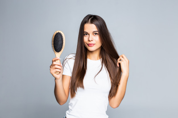 Foto de fundo cinza com mulher de pele clara usando blusa branca mostrando escova de cabelo 