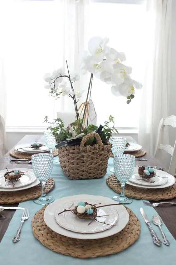 mesa posta azul para Páscoa com arranjo de orquídea branca e decoração de ninho com ovos
