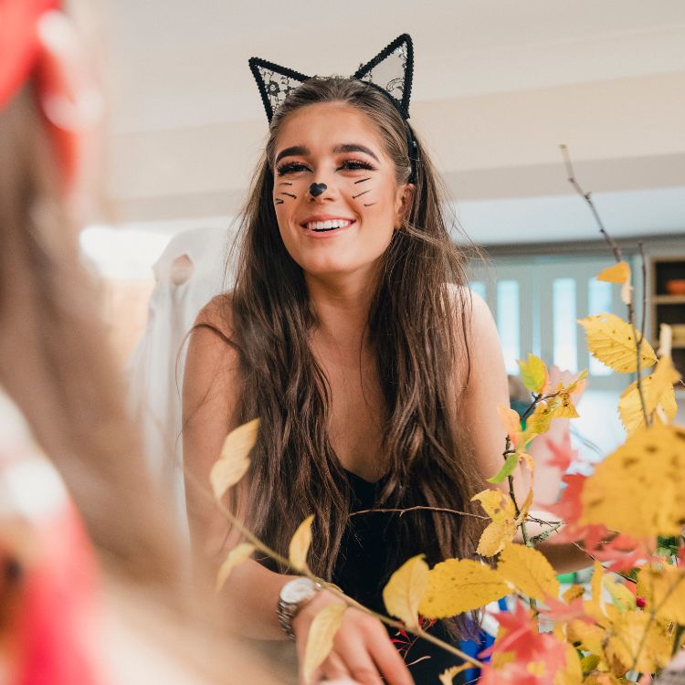 Mulher de pele clara usando fantasia de gatinho, com tiara de orelhas e maquiagem facial fofa