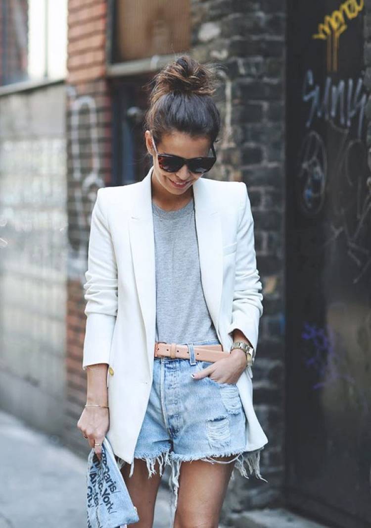 Mulher de pele clara usando camsieta cinza, blazer branco e shorts jeans destroyed
