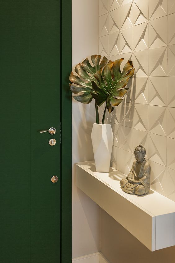Hall branco com porta verde, parede com azulejo 3D, aparador branco suspenso, estátua de Buda e vaso branco com costela-de-adão