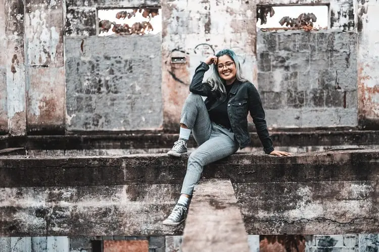 garota posando sentada em uma mureta, usando jaqueta jeans escura e calça cinza
