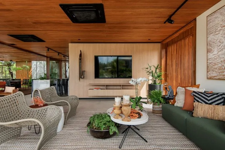 Plantas dispostas em sala de estar em madeira, com mesa de centro branca, sofá verde e poltronas cinzas. 