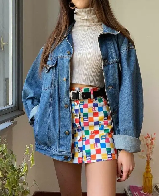 Look cropped gola alta, jaqueta jeans e saia xadrez colorida. 