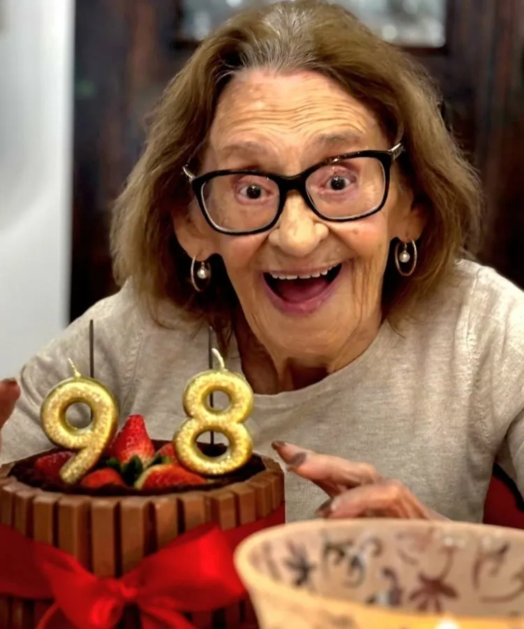 Atriz Laura Cardoso em frente a mesa com bolo e velas de 98 anos
