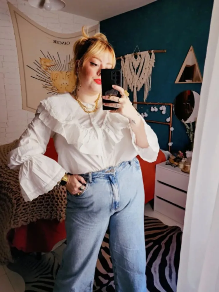 Mulher de pele clara de camisa branca d babados e calça jeans 