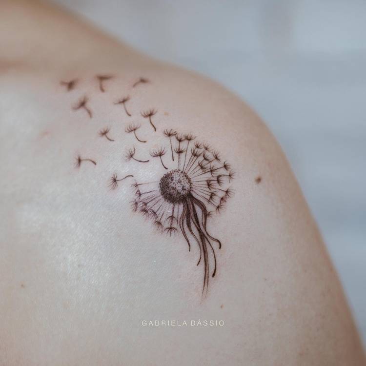 Mulher de pele clara com ombro tatuado com dente de leão ao vento, em fine line e sombra