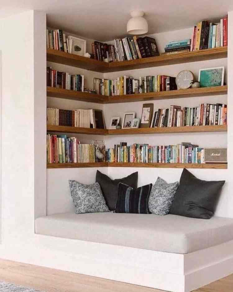 cantinho com banco branco, almofadas pretas e prateleiras com livros