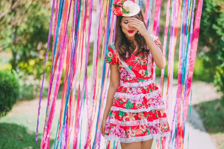 Mulher de pele clara usando vestido vermelho floral com rendas e chapéu de palha