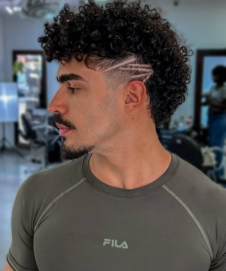 Um homem de perfil com cabelo crespo e cacheado, penteado em um mullet moderno. As laterais têm um high fade, com um design de linhas raspadas acima da orelha, e a parte de trás é mais longa e volumosa.







