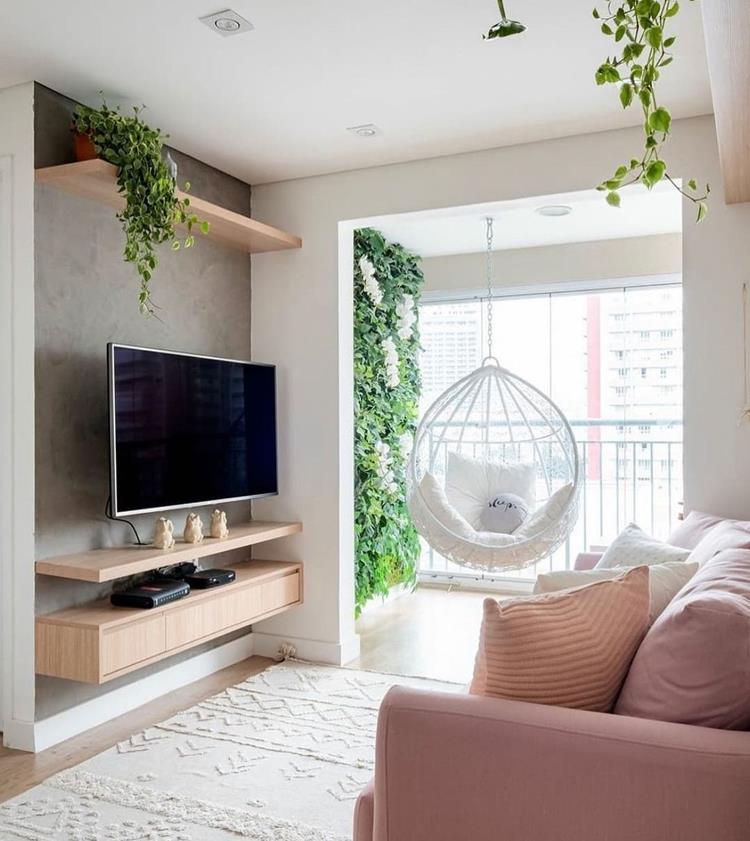 foto de sala pequena com parede cimento queimado, rack suspenso de madeira, tapete bege e sofá rosa, tudo integrado com varanda com jardim vertical e balanço redondo