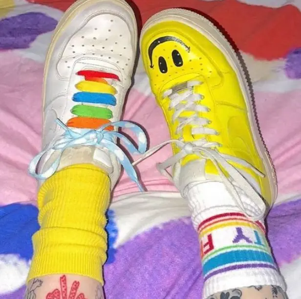 Tênis customizados inspirados na estética kidcore, o esquerdo com cadarço colorido e o direito com smile