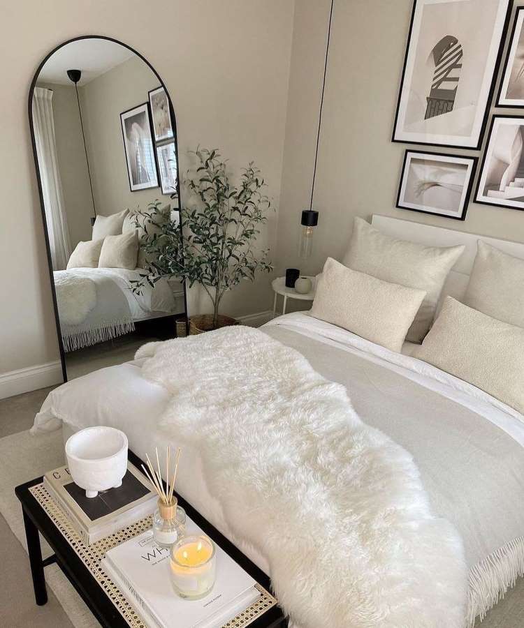 Quarto de casal com espelho grande apoiado na parede. Cores predominantes: branco, off-white e preto
