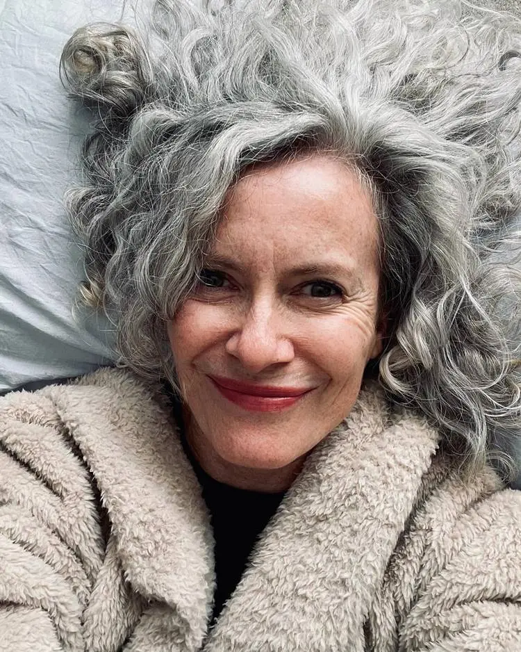 Mulher grisalha sorridente deitada na cama