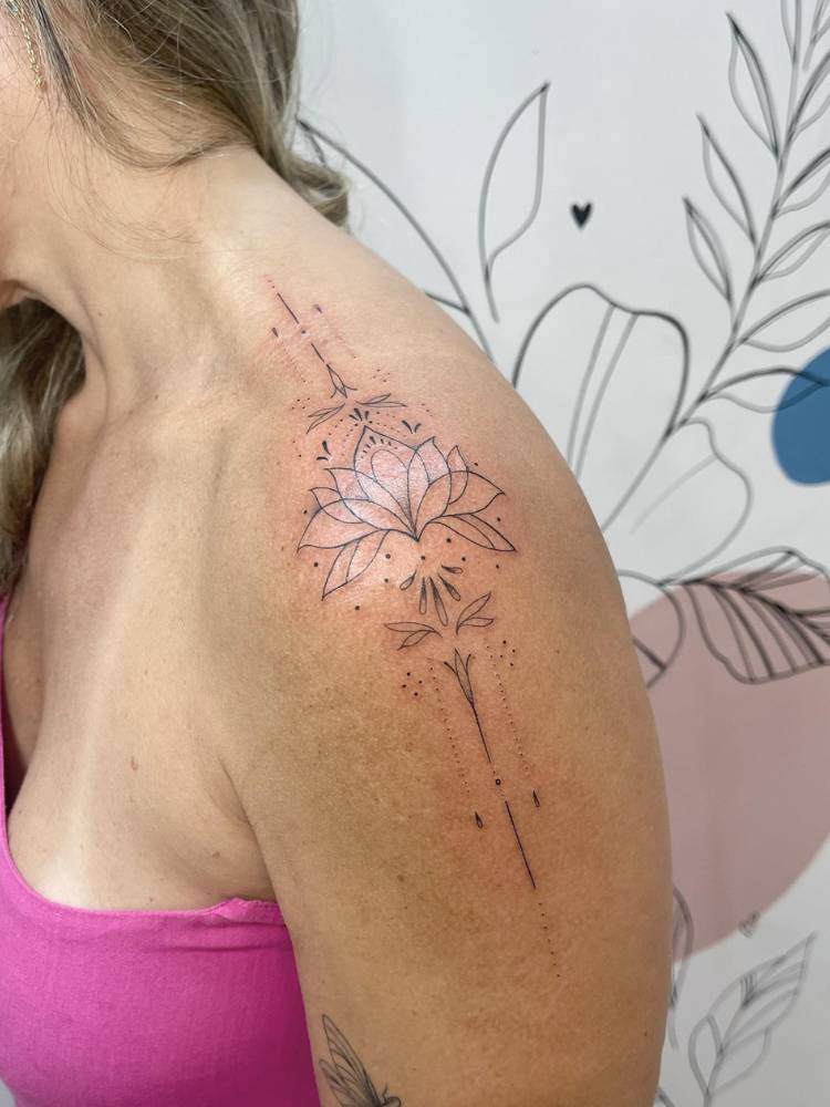 Mulher de pele clara de lado, usando blusa rosa e com tatuagem de lírio no ombro, com linhas e ornamentos