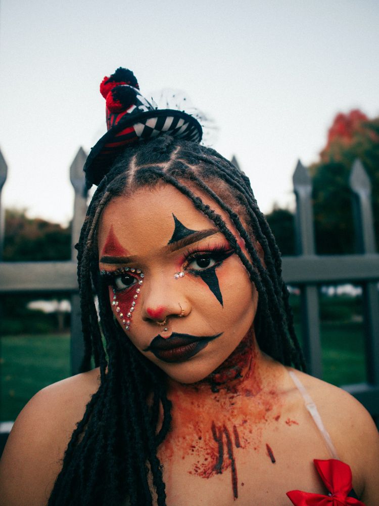 Mulher de pele negra com maquiagem de palhaço e sangue falso no pescoço e colo