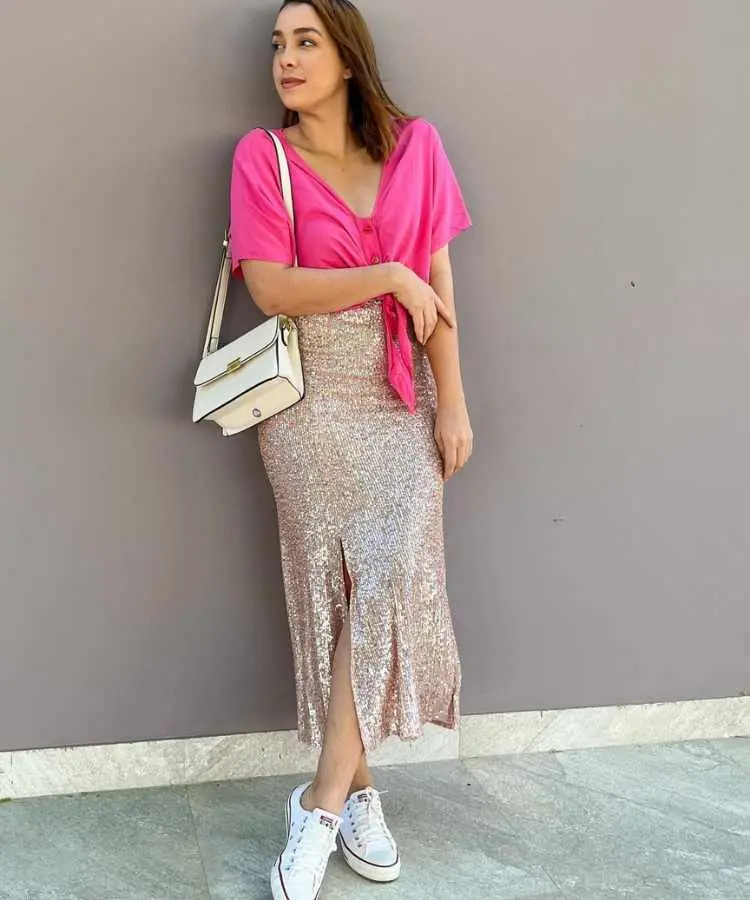 Mulher com top rosa e saia brilhosa.