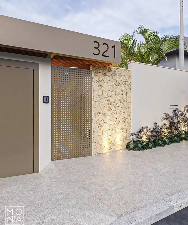Fachada com muro moderno simples em tons bege, portão metálico perfurado dourado e detalhe em pedra natural iluminada. Número "321" em destaque na estrutura lisa. Paisagismo com plantas verdes, calçada pavimentada em tom claro e céu parcialmente nublado.
