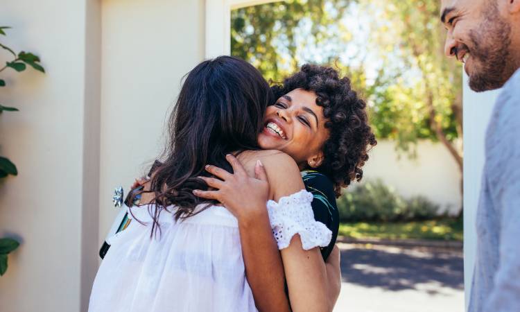 Duas mulheres de abraçando e homem olhando.