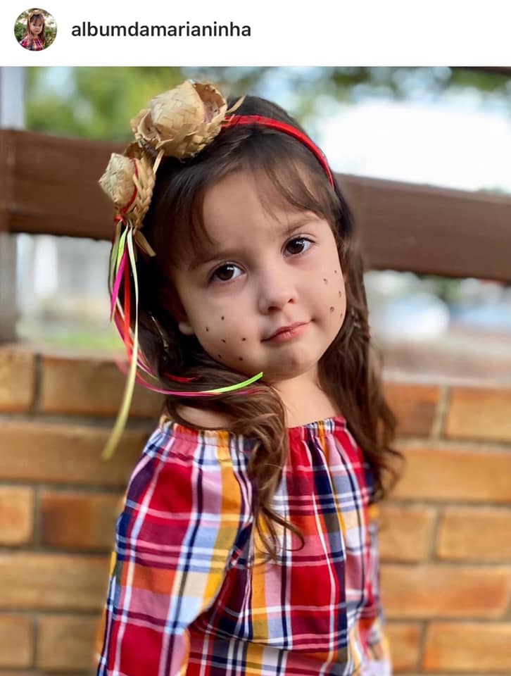 Foto de garotinha com maquiagem de festa Junina com sardas e tiara decorada com fitas e chapéu de palha