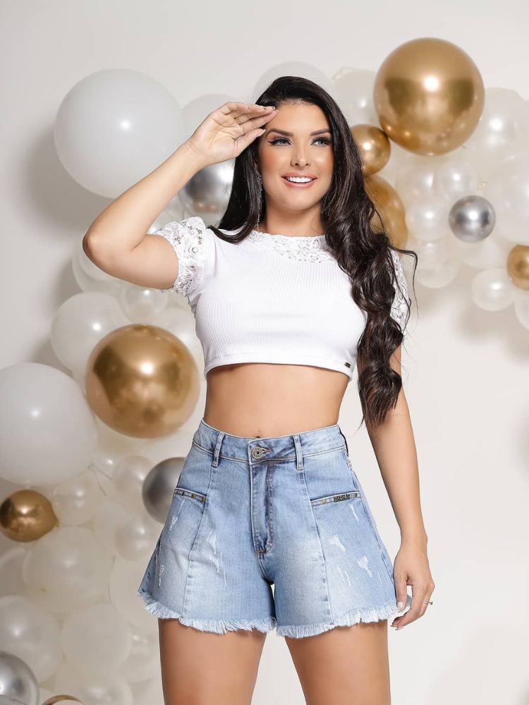 Mulher de pele clara usando cropped branco e shorts jeans godê