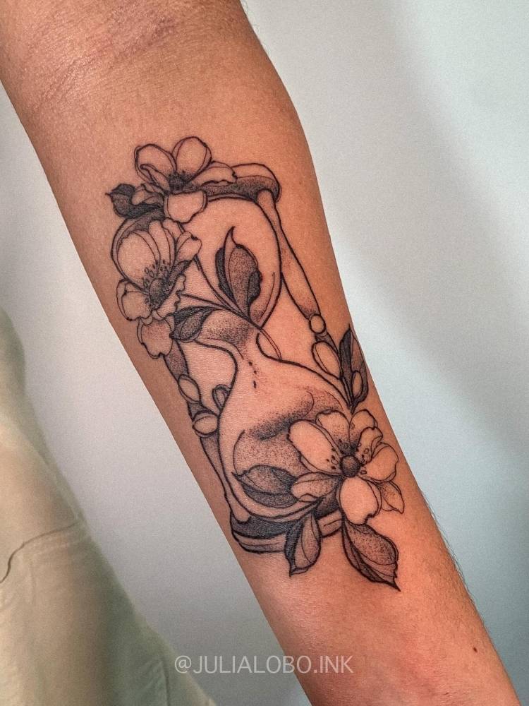 Braço com tatuagem de ampulheta com flores e sombras