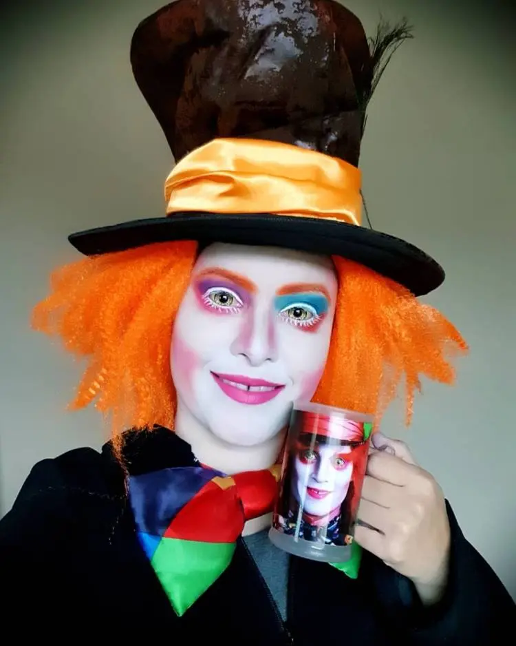 Pessoa com fantasia e maquiagem de Chapeleiro Maluco, com sombra azul e roxa, batom rosa e sobrancelha ruiva