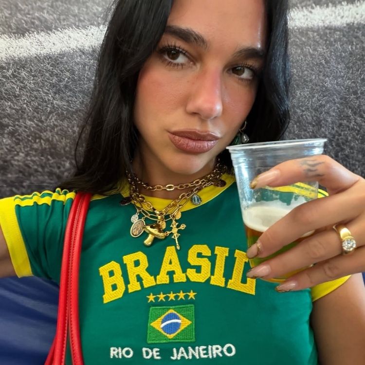 Foto de Dua Lipa vivendo o sonho brasileiro com blusa verde e amarela e copo de cerveja