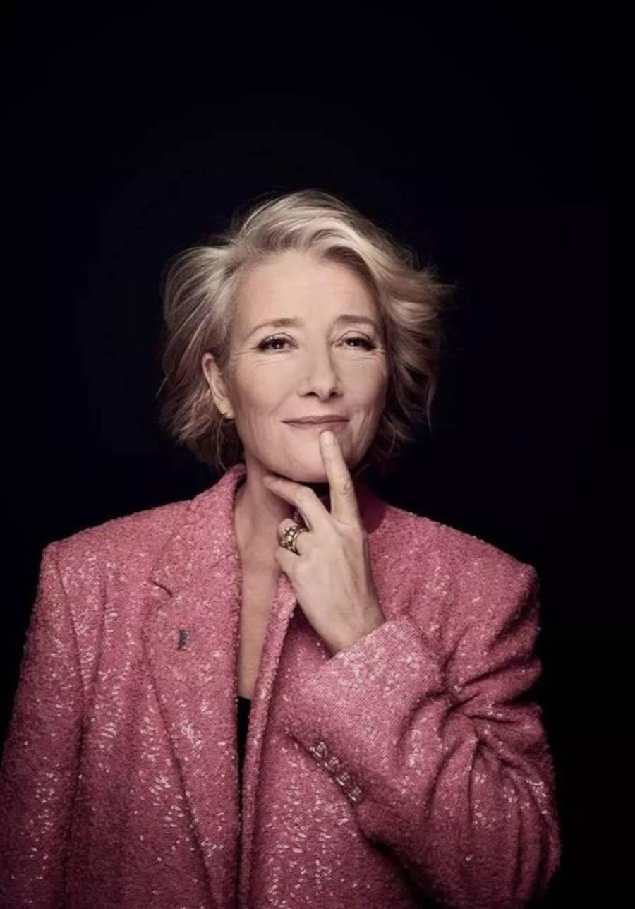 Foto da atriz Emma Thompson vestindo um blazer rosa com glitter e com o fundo preto