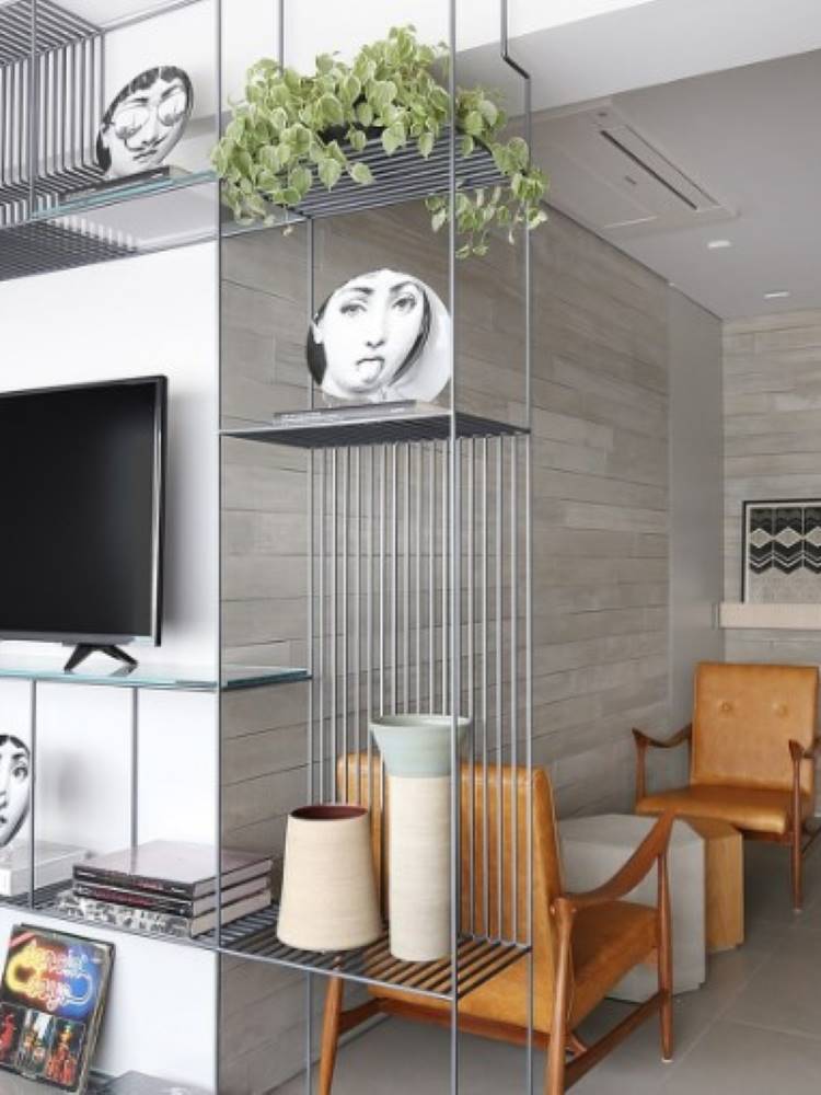 Estante vazada feita de aço, com TV, pratos de porcelana, vaso de planta, vasos e outros itens decorativos. 