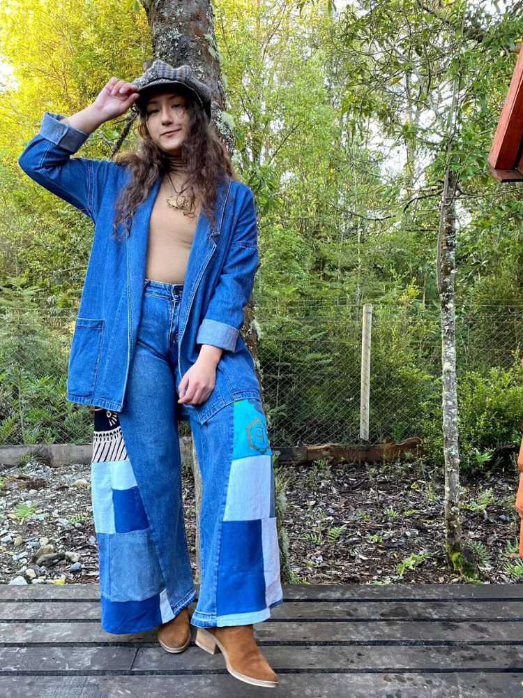 Mulher de pele clara próxima às árvores usando jaqueta jeans, blusa rosa e calça jeans com patchwork