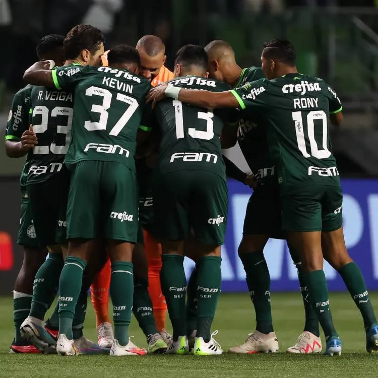 Elenco do Palmeiras usando o primeiro uniforme (verde escuro) se abraçando no gramado.