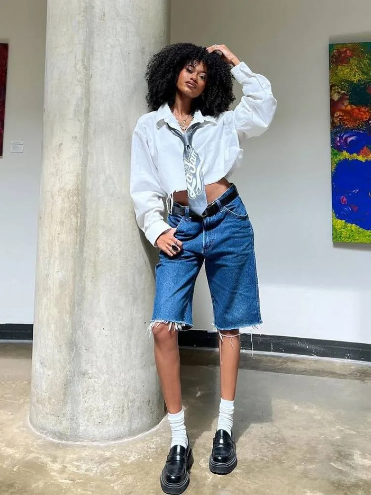 mulher usando gravata, camisa cropped, bermuda jeans e mocassim