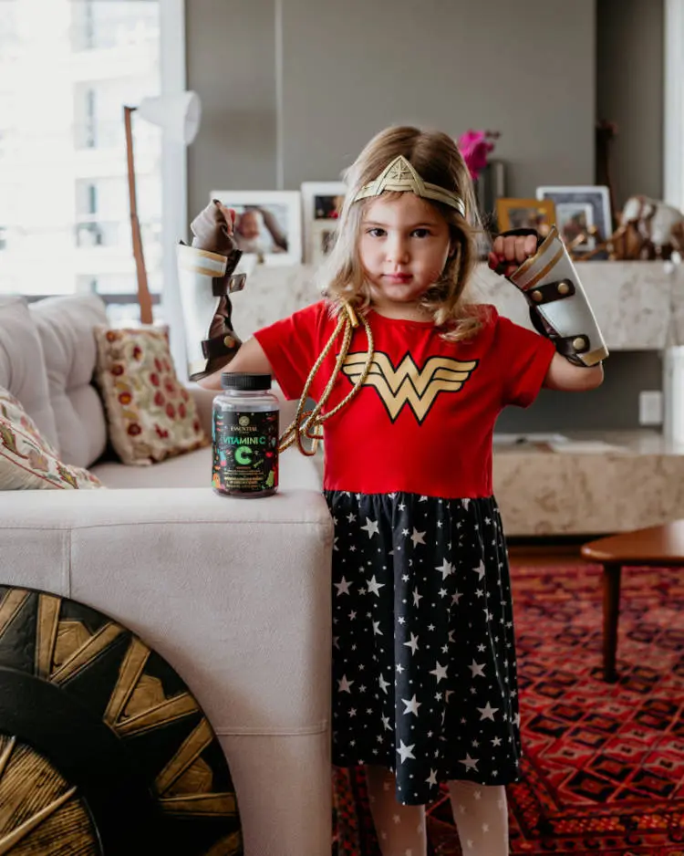 Criança com roupa da Mulher Maravilha e pote de Vitamina C.