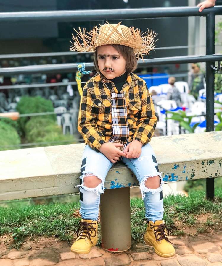 Menino usando camisa xadrez amarela, calça jeans e chapéu de palha.
