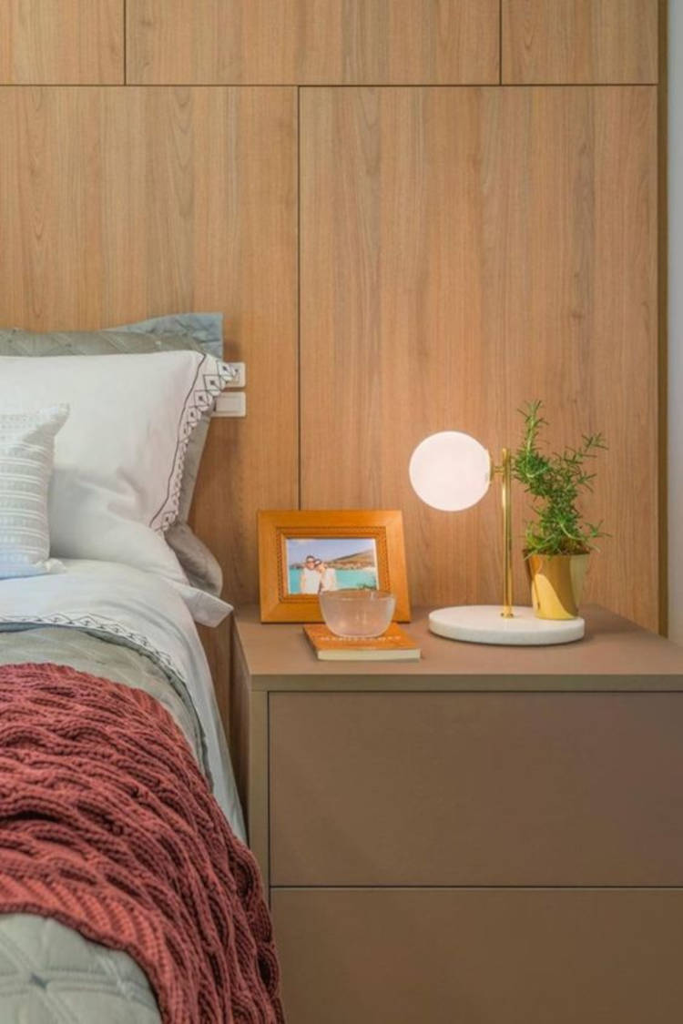 Zoom em quarto de casal com parede de madeira, mesa de cabeceira marrom, luminária