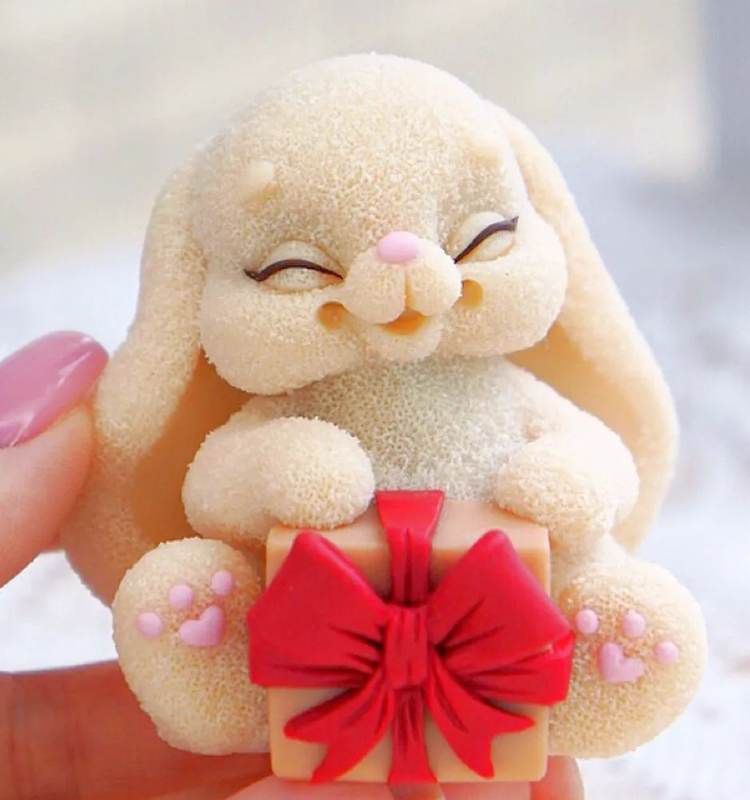 Coelhinho fofinho de biscuit, segurando presentinho com laço vermelho.